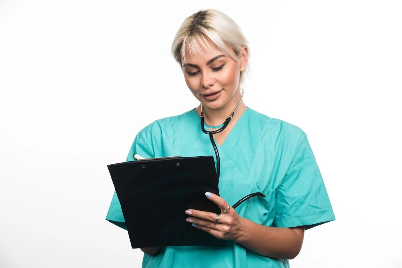 Женщина-врач пишет что-то ручкой на планшете с зажимом на белой поверхности.